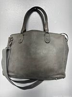 Front side of the grey Roots genuine leather handbag with handles and adjustable strap.