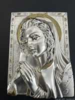 Front view of silver-plated Virgin Mary plaque showing detailed facial features, hands in prayer, gold-tone halo, and decorative border.