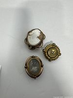 Top view of three Victorian brooches: carved cameo, mourning photograph, and pearl-accented star brooch.