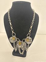 Front view of the silver-tone mixed metal necklace with three flower elements and yellow resin stones on a black display stand.