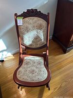 Front view of antique rocking chair showing carved wooden frame and floral embroidered upholstery.