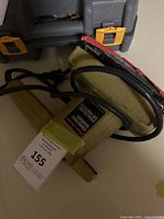 Electric hand sander laid on its side showing label and attached sanding paper with the cord wrapped around the body.