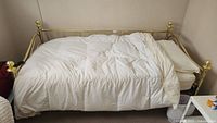 Side view of brass day bed dressed with white bedding and mattress, room corner background.