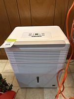 Front view of white dehumidifier showing horizontal slats, water indicator, and attached orange power cord.