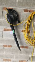 Side view showing handle, body and attached yellow power cord of the electric leaf blower.