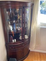 Full view of the dark stained solid wood corner china cabinet with glass doors displaying various glassware and ceramic items inside.