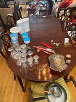 Full view of dining table with several chairs arranged around it. Various non-related items are placed on the table.