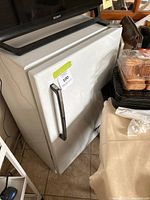 Side view of white mini freezer with a handle, showing dents on the exterior.