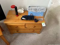 Front angle view of solid pine wood dresser showing four drawers and items placed on top for scale.