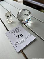 Photo of the two items: a small crystal owl figurine and a large faceted crystal sphere on a white surface with auction lot number card.