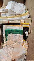 Top down photo of folded assorted table linens in assorted colors including white, cream, yellow, green, black, some with lace and embroidered details