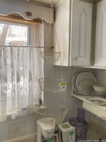 Full view of the three-tier vintage metal hanging basket in a kitchen environment, showing it hanging in front of a window.