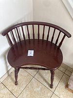 Front angled view of vintage wooden chair showing curved backrest with spindles, kidney-shaped seat, and turned legs with some scratches and wear on wood finish.