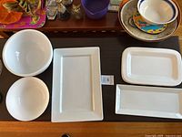 Five white ceramic serving items on a table: two round bowls and three rectangular platters of varying sizes.