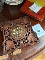 Top angle photo showing carved floral details of wooden trivet and mother of pearl inlay center.
