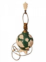 Full view of vintage Aladdin Alacite table lamp showing green and white floral relief glass body, brass socket, and finial with attached cord.