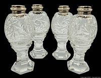Four vintage crystal shakers with a hexagonal pedestal base and sterling silver mother of pearl tops, arranged upright against a black background.