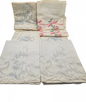 Four pairs of folded embroidered pillow cases arranged flat showing two different embroidered floral designs, some cases have pink and green embroidery, others have blue and peach embroidery.