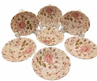 Front view of seven Johnson Bros Rose Chintz bowls arranged in a semicircle, showing floral pattern and scalloped edges.