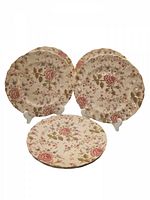Six vintage Johnson Bros rose chintz floral patterned dinner plates displayed on stands and stacked, showing the full pattern and scalloped edges.