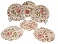 Six vintage Johnson Bros Rose Chintz tea plates arranged with three standing on display easels and three lying flat, showing overall pattern and scalloped edges.