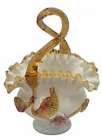 Front angled view of the white hand blown glass basket with ruffled edge, amber twisted handle, and applied amber and pink glass decorations.