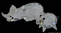 Clear faceted crystal rhinoceros and pig figurines, side view showing size difference and details.
