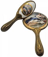 Two-piece antique dresser set, hand mirror and brush with decorative porcelain backs and gold-tone floral engraved handles.