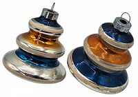 Two multi-tiered swirl-shaped vintage glass Christmas ornaments in metallic silver, orange, and blue colors, lying on a white background. Show top caps and hanging rings.