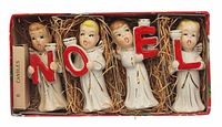 Front view of open box showing four porcelain angels and candles pack on straw bedding