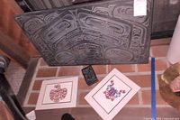 Overall view: black carved relief panel leaning on brick hearth with two matted prints below