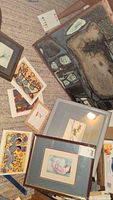 Photo showing multiple artworks spread on carpet including one large framed abstract painting and several smaller prints and framed pieces