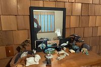 Overall view of black wood-framed rectangular mirror on table with various animal-themed sculptures and decorative art pieces