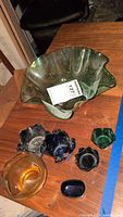 Top view of large green ruffled glass bowl and smaller colored bowls on wooden surface, dusty and uncleaned.
