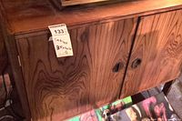 Front view of two-door wooden cabinet showing woodgrain veneer, round carved handles and MaxSold sticker with dimensions