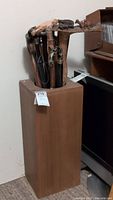 Overall view of tall wooden cane holder containing multiple canes with visible carved wooden handles and variants.