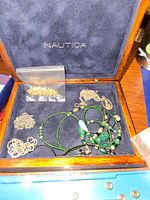 Wooden Nautica jewelry box containing various gold-tone chains, green beaded necklaces, and pendants.