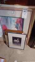 Six framed art pieces stacked/arranged on floor including the signed swan print