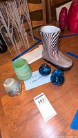Photo of the various glass art pieces arranged on a wooden table including the rain boot vase, small blue orbs, and others.