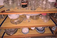 Top and second shelf showing clear glass bowls, tumblers and small dessert dishes, white plates below