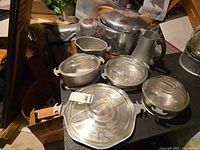 Full overview of the set showing multiple aluminum pots with lids and a large pressure cooker with wooden handles on a black table.