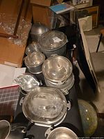 Overview of various aluminum pots, trays, and glass lids arranged on a table showing the lot contents