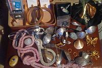 Photo showing jewelry assortment including wooden bangles, pink beaded strands, various pins and brooches, and gold-tone flower-shaped earrings and brooches placed inside the jewelry case.