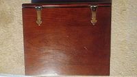 Closed view of rectangular polished wooden box with brass hinges on carpet.