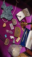 Photo showing carved stone pendant, paw print pendant, various belt buckles, money clips, coral/gemstone ring, turquoise pieces, guitar pick, decorative feathers, small bell-shaped cup, and Fisher Space Pens.