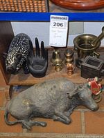 Photo showing black hand-shaped dish and various small metal bells with large metal bull figurine on brick floor