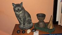 Cast iron cat sculpture on wood surface with three natural stones in front and decorative metal pieces on a green tray alongside.