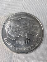 Close-up image of silver-tone coin medallion showing embossed astronaut profiles and lettering.