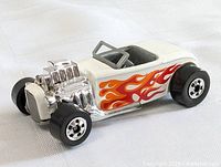Close-up side angled view of the white Hot Wheels roadster toy car with flames, showing chrome engine and black wheels with silver rims.