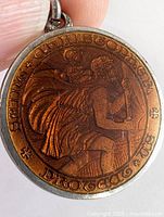 Close-up showing detailed engraving of Saint Christopher carrying a child with surrounding embossed text on copper-toned section and sterling silver border, held by fingers for scale.